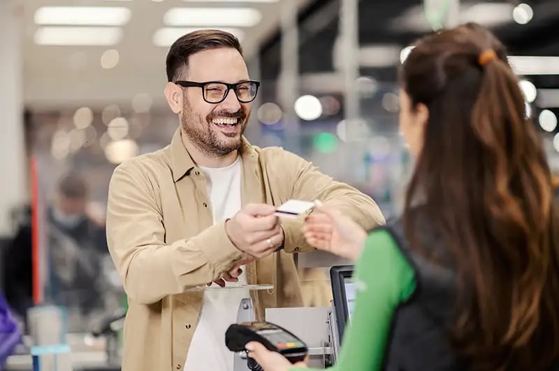 man handing a woman his credit card in a checkout lane